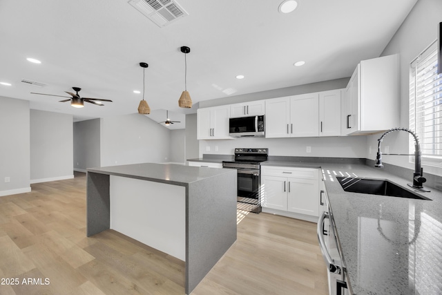 kitchen featuring sink, appliances with stainless steel finishes, white cabinetry, a center island, and light stone counters