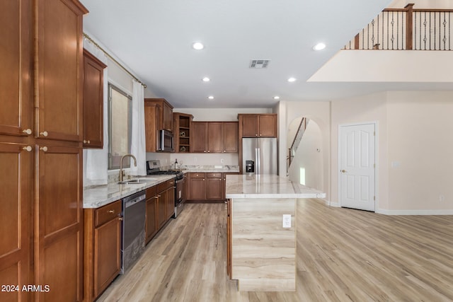 kitchen featuring light hardwood / wood-style flooring, sink, a center island, appliances with stainless steel finishes, and light stone counters