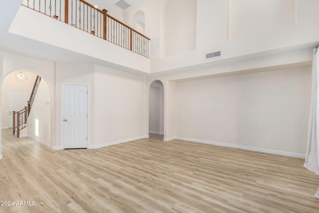 unfurnished living room with a towering ceiling and light wood-type flooring