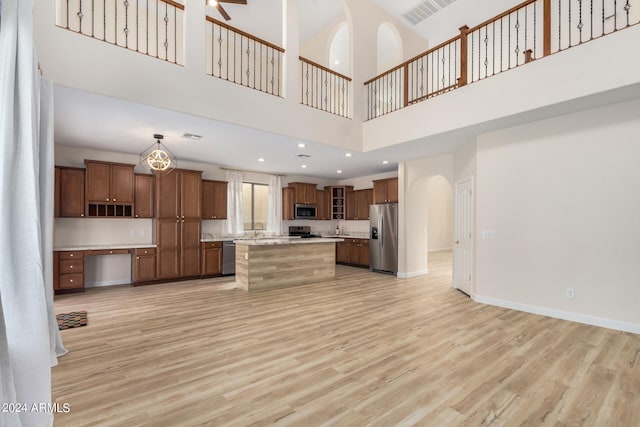 kitchen with a kitchen island, appliances with stainless steel finishes, light hardwood / wood-style flooring, a towering ceiling, and decorative light fixtures