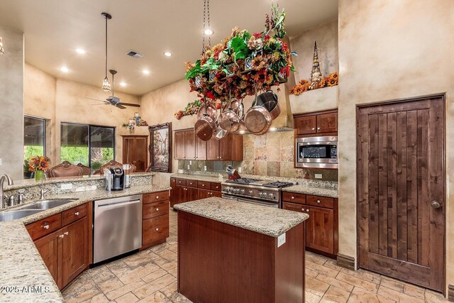 kitchen featuring appliances with stainless steel finishes, hanging light fixtures, ceiling fan, a kitchen island, and sink