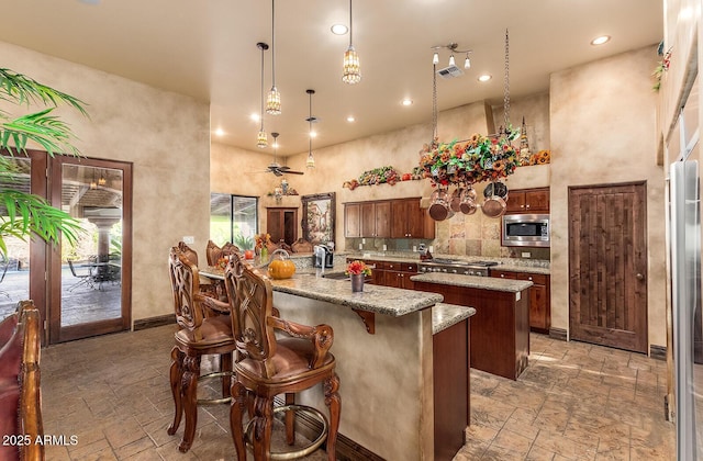 kitchen featuring appliances with stainless steel finishes, hanging light fixtures, a center island, light stone counters, and sink