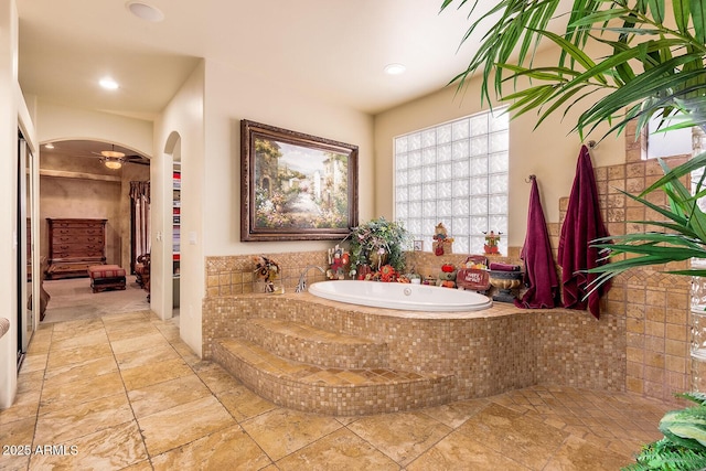 bathroom featuring a relaxing tiled tub and ceiling fan