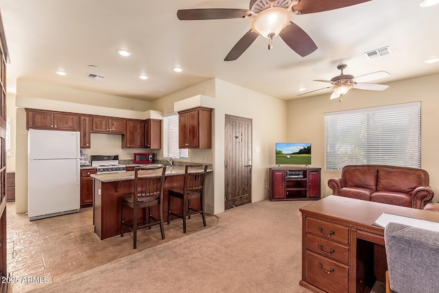 kitchen with white appliances, a kitchen bar, light carpet, ceiling fan, and light stone countertops