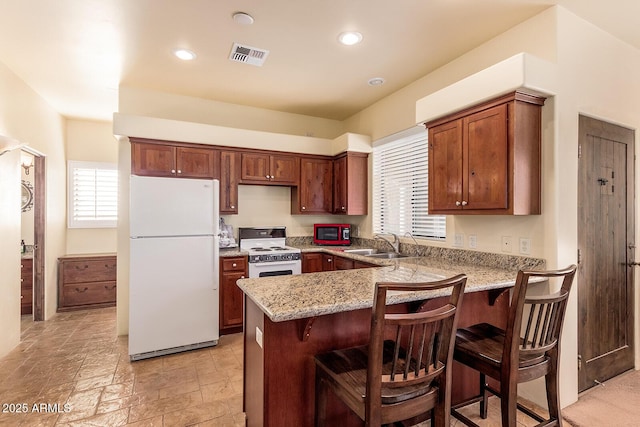 kitchen with white appliances, kitchen peninsula, light stone countertops, a kitchen breakfast bar, and sink