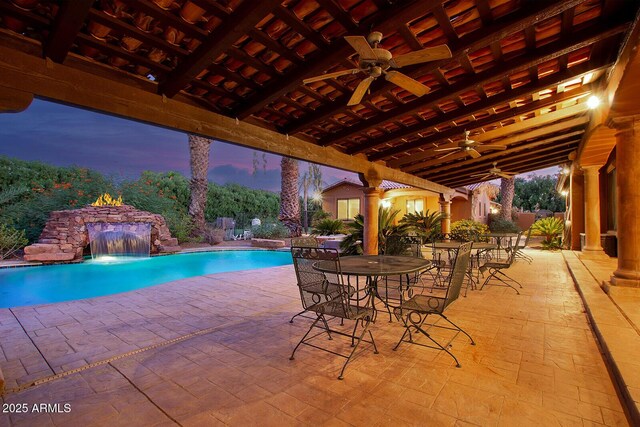 pool at dusk with ceiling fan, pool water feature, and a patio area