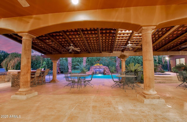 patio terrace at dusk with pool water feature, grilling area, ceiling fan, and exterior bar