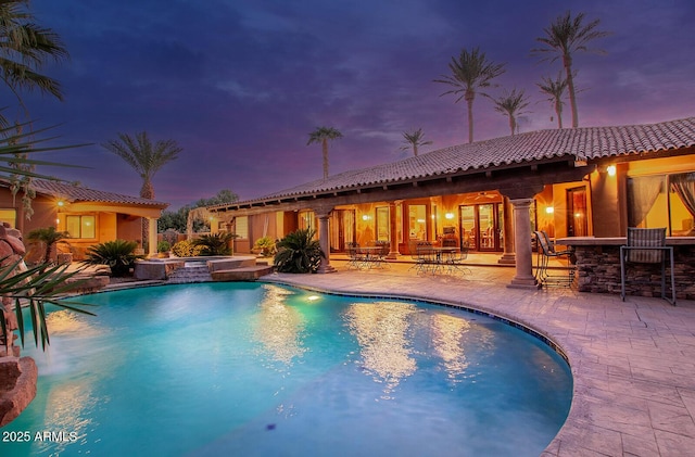 pool at dusk featuring a patio area and a bar