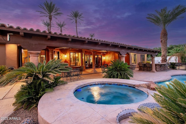 pool at dusk featuring an outdoor bar, a patio area, and an in ground hot tub