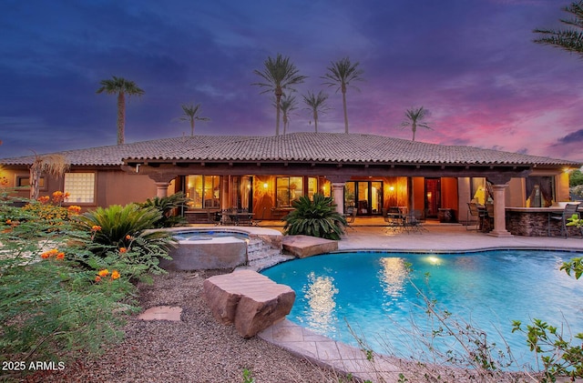 pool at dusk with a patio area, a bar, and an in ground hot tub