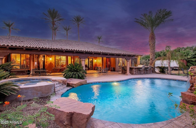 pool at dusk featuring a patio and an in ground hot tub