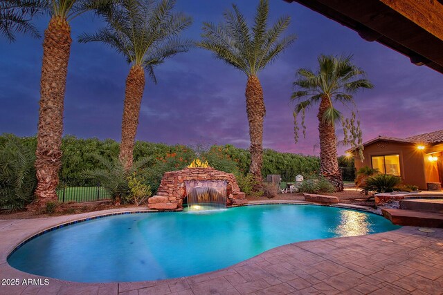 pool at dusk with pool water feature, an in ground hot tub, and a patio