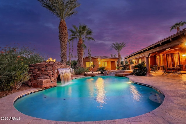 pool at dusk featuring pool water feature and a patio area