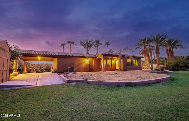 back house at dusk with a patio, central AC unit, and a lawn