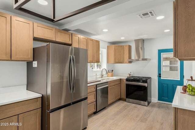 kitchen featuring visible vents, light wood-style flooring, a sink, appliances with stainless steel finishes, and wall chimney range hood