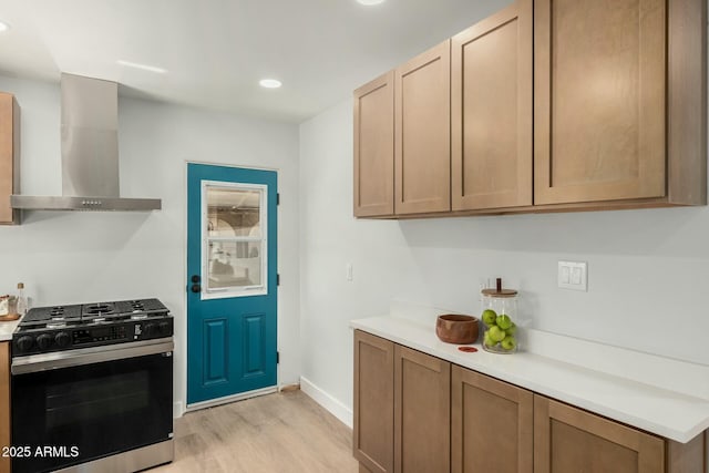 kitchen featuring light wood-style flooring, wall chimney range hood, gas range oven, recessed lighting, and light countertops