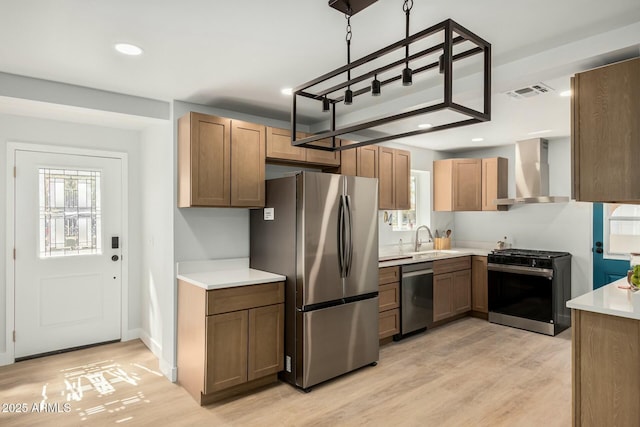 kitchen with visible vents, a sink, stainless steel appliances, light countertops, and wall chimney range hood