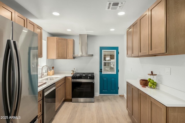 kitchen featuring visible vents, appliances with stainless steel finishes, light wood-style floors, wall chimney exhaust hood, and a sink