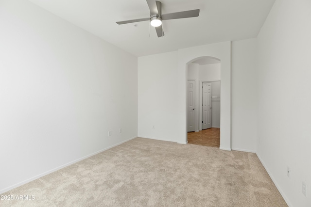 carpeted spare room with arched walkways, a ceiling fan, and baseboards