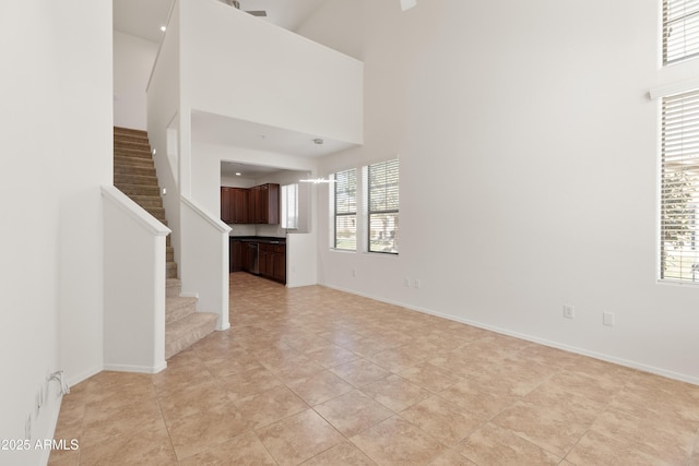 unfurnished living room featuring stairs, baseboards, a towering ceiling, and a healthy amount of sunlight