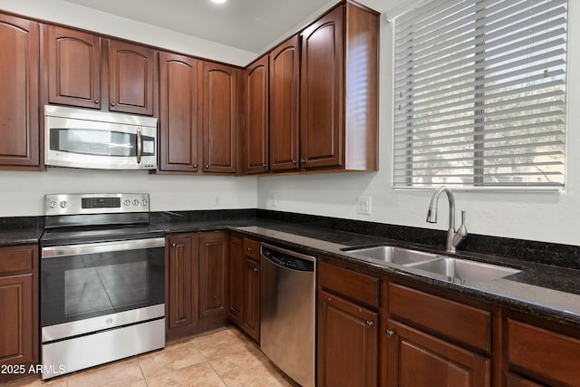 kitchen featuring stainless steel appliances, a sink, dark stone countertops, and light tile patterned floors