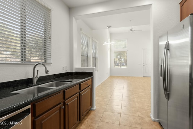 kitchen with light tile patterned floors, ceiling fan, stainless steel appliances, a sink, and dark stone counters