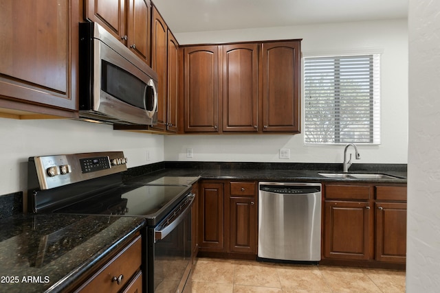 kitchen with dark stone counters, stainless steel appliances, a sink, and light tile patterned flooring