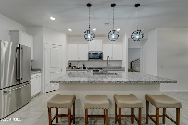 kitchen with stainless steel appliances, white cabinetry, hanging light fixtures, and a center island with sink