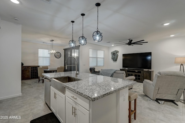 kitchen featuring sink, hanging light fixtures, an island with sink, light stone countertops, and white cabinets