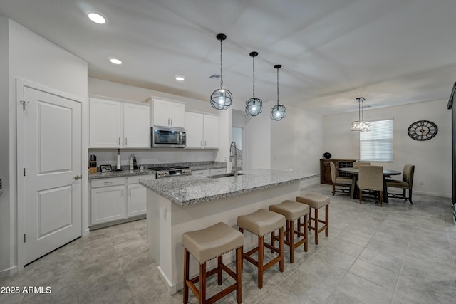 kitchen featuring sink, white cabinets, hanging light fixtures, a kitchen island with sink, and light stone countertops