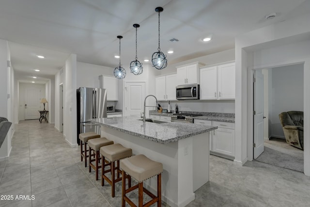 kitchen with stainless steel appliances, an island with sink, and white cabinets