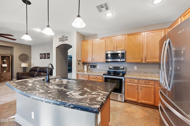 kitchen with appliances with stainless steel finishes, pendant lighting, an island with sink, sink, and dark stone countertops