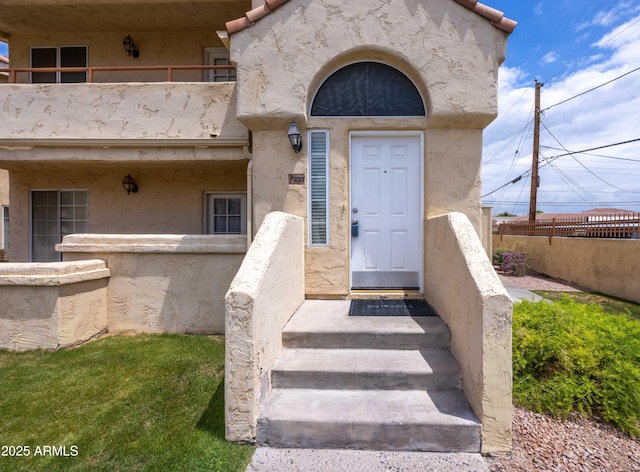 entrance to property featuring a balcony, stucco siding, and fence