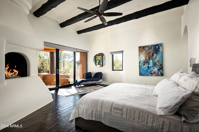 bedroom featuring access to outside, ceiling fan, beamed ceiling, a large fireplace, and dark hardwood / wood-style flooring