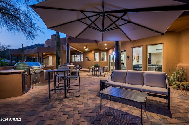 patio terrace at dusk featuring area for grilling, an outdoor living space, and an outdoor kitchen