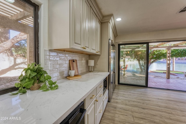 kitchen with backsplash, a wealth of natural light, light hardwood / wood-style flooring, and a water view