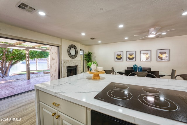 kitchen with light stone countertops, ceiling fan, black electric stovetop, light hardwood / wood-style floors, and a fireplace