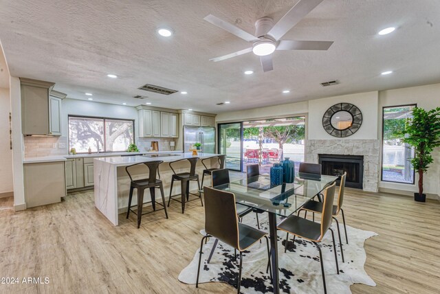 dining area featuring a fireplace, a textured ceiling, light hardwood / wood-style flooring, and ceiling fan