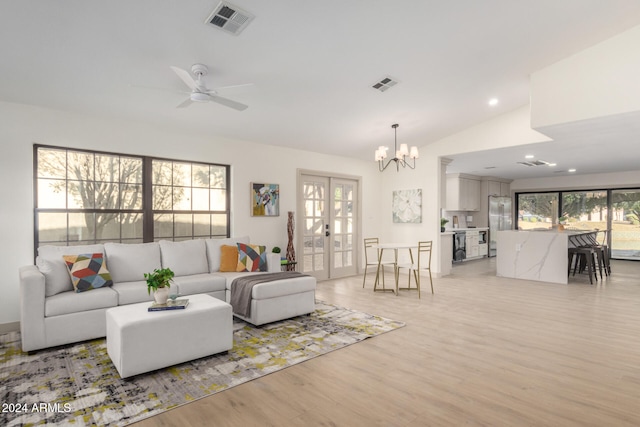 living room with light hardwood / wood-style flooring, ceiling fan with notable chandelier, a healthy amount of sunlight, and vaulted ceiling