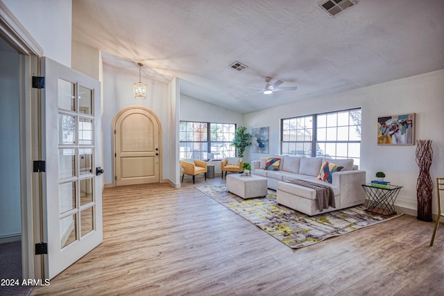 living room featuring ceiling fan with notable chandelier, a textured ceiling, light wood-type flooring, and lofted ceiling