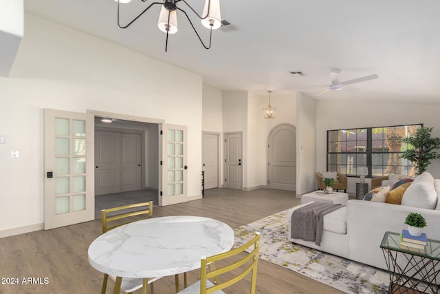 living room featuring french doors, ceiling fan with notable chandelier, hardwood / wood-style flooring, and high vaulted ceiling