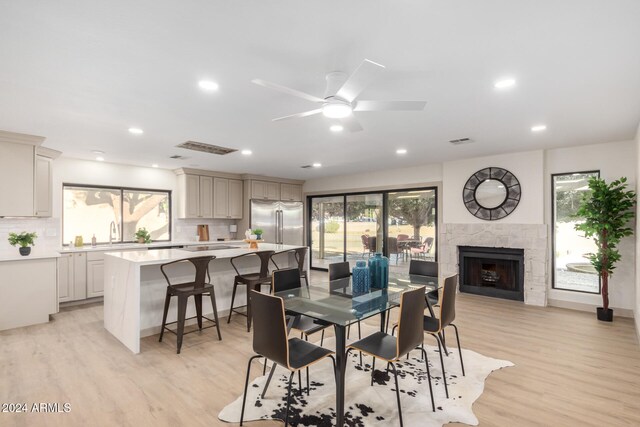 dining room featuring ceiling fan, sink, a fireplace, and light hardwood / wood-style flooring