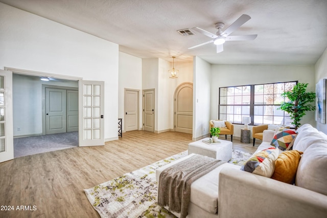 living room featuring ceiling fan with notable chandelier, light hardwood / wood-style floors, a textured ceiling, and high vaulted ceiling