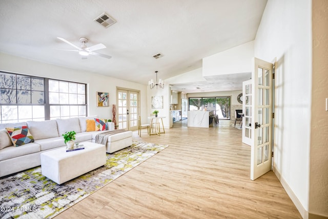 living room with ceiling fan with notable chandelier, light hardwood / wood-style flooring, high vaulted ceiling, and french doors