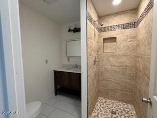 bathroom featuring toilet, vanity, a tile shower, and tile patterned flooring