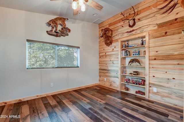 spare room with wooden walls, ceiling fan, and dark wood-type flooring