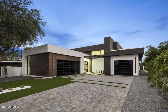 view of front of property featuring a front lawn, fence, stucco siding, decorative driveway, and a garage