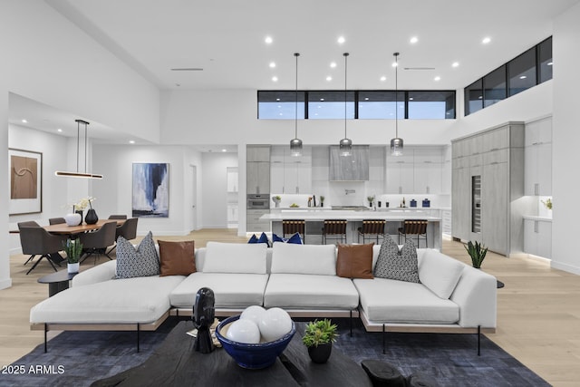 living area featuring a high ceiling, recessed lighting, light wood-style floors, and baseboards