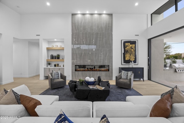 living room with built in features, recessed lighting, wood finished floors, and a towering ceiling