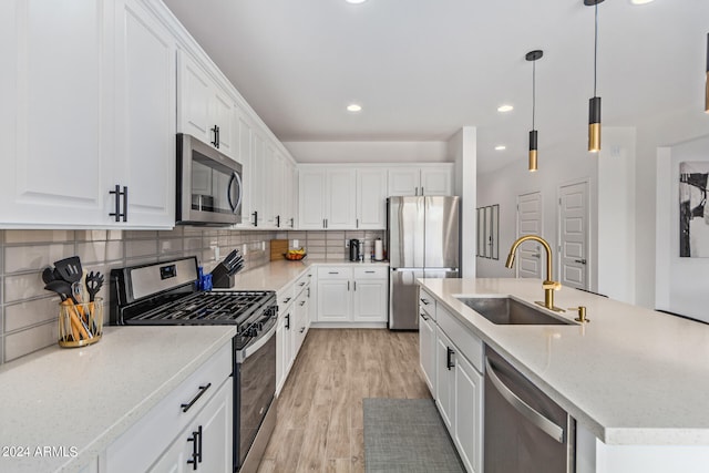 kitchen featuring appliances with stainless steel finishes, white cabinets, light hardwood / wood-style flooring, a center island with sink, and sink